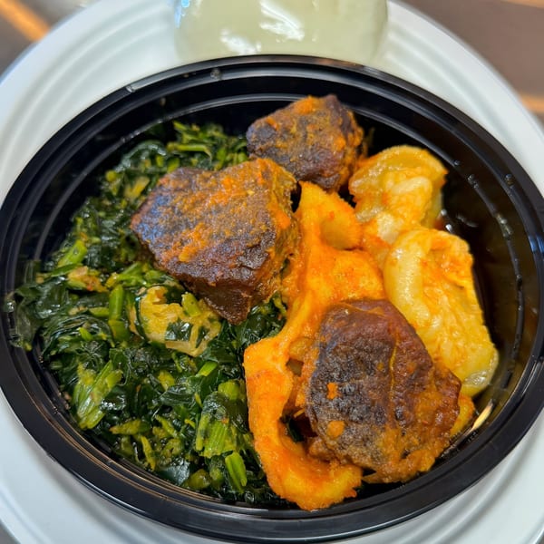 A Nigerian dish with stewed meat, green vegetables, and yellow yam in a black takeout container.